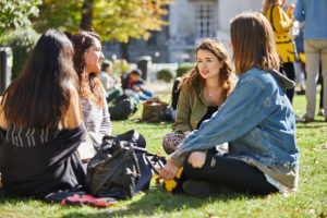 A group of four students sat on the grass in a park on a sunny day