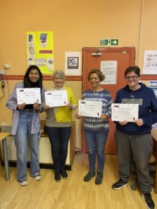 Four workshop participants smiling and holding their certificates of completion. 