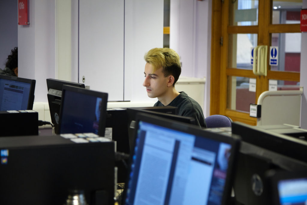 Photo of a white male student working at one of the many computers in the Library.