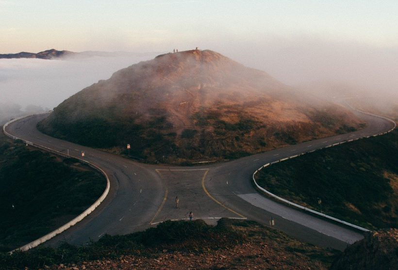 A highway splits around a small hill. Mist and mountains visible in the distance.
