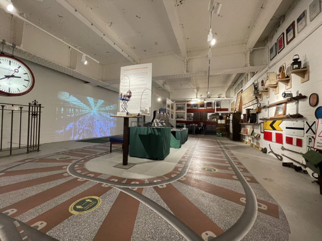 Interior of Glasgow Central Station Museum. On the left wall is a large illuminated station clock, and on the right wall are lamps, signals and other objects.