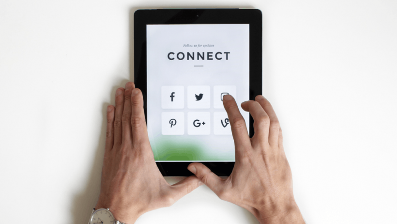 Hands holding a tablet computer. On the screen is the word 'connect' with a grid of social media icons