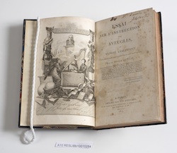 Book open on frontispiece, left hand side is an image of two blind students, right hand side is book information